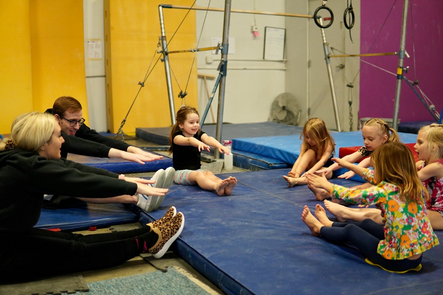 Bambini e adulti che si allungano su tappetini blu in uno studio di ginnastica.